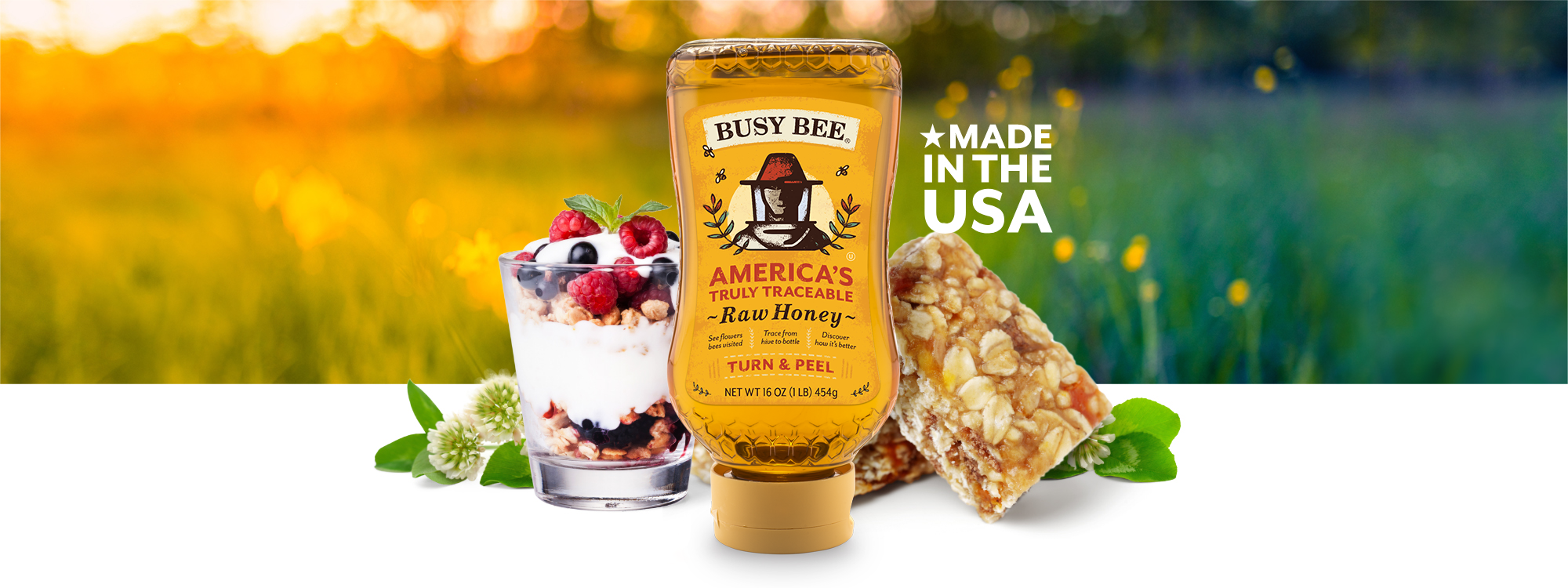 yogurt parfait, granola bars and a bottle of Busy Bee Honey in the foreground. Busy Bee Unfiltered Raw Honey Made in the U.S.A.  Sunny field in background